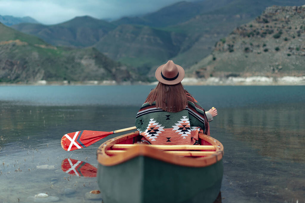 Girl canoeing on a lake in the mountains on a cloudy day. Moody atmosphere on Lake Gizhgit in the village of Bylym, Kabardino-Balkaria - Photo, Image