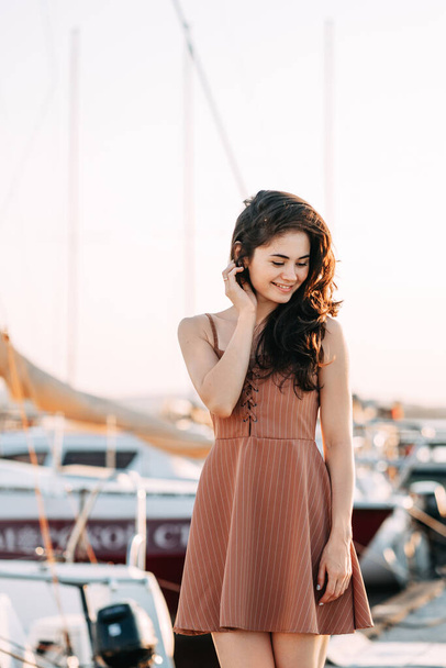 young beautiful healthy woman walks along the pier against the background of the yacht pier. Sea port in summer. A weekend trip. sunset sun, golden hour, smile - Foto, Imagen
