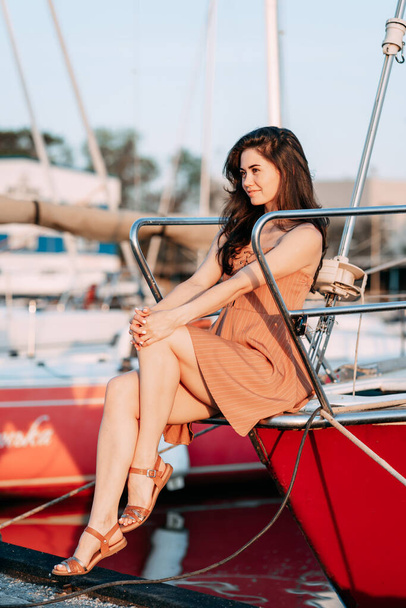 young girl in a dress sits on a boat on a pier on the sea in the summer evening, the setting sun, vacation - Фото, зображення