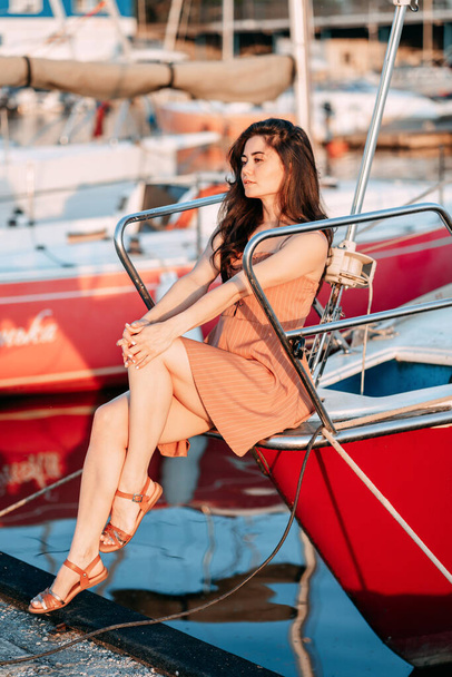 niña en un vestido se sienta en un barco en un muelle en el mar en la noche de verano, el sol poniente, vacaciones - Foto, Imagen