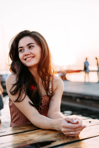 young beautiful smiling woman sits at a wooden table - Photo, Image
