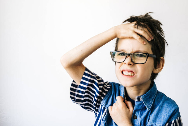Autism and Invisible Illness concept. Portrait of autism boy with glasses grimaces on a white wall backdrop. Children head pain - Фото, зображення
