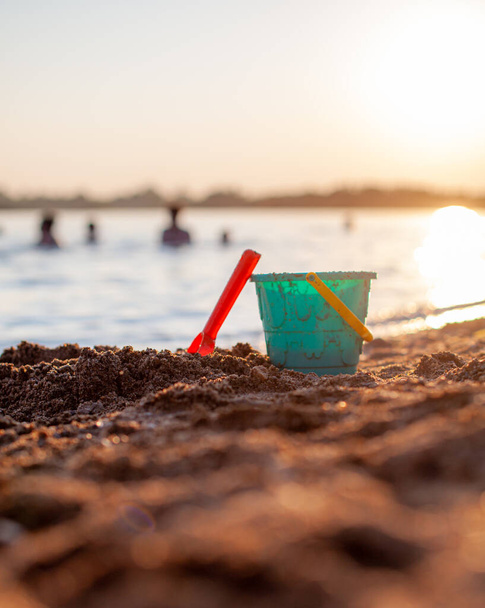 Children's toys for playing on the sand. Plastic bucket and rake on the beach at sunset. The concept of summer, family holidays and vacations. - Fotografie, Obrázek