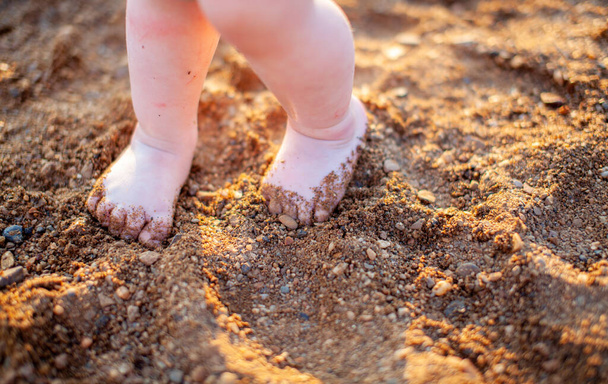 Gyermek mezítláb nyáron egy arany homokos strandon közelkép. A gyermekbiztonság fogalma. A gyermekekkel való kikapcsolódás fogalma. - Fotó, kép