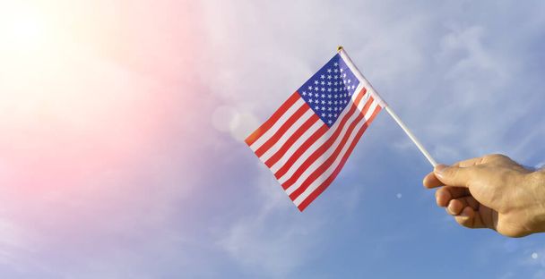 Amerikai zászló a kézben. Ünnepi amerikai zászló a kezében a kék ég és a nyári természeti táj ellen. Amerikai ünnepek koncepciója. - Fotó, kép