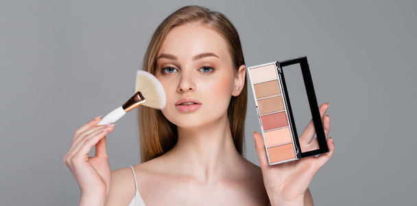young woman holding cosmetic brush and blush palette isolated on grey, banner - Фото, зображення