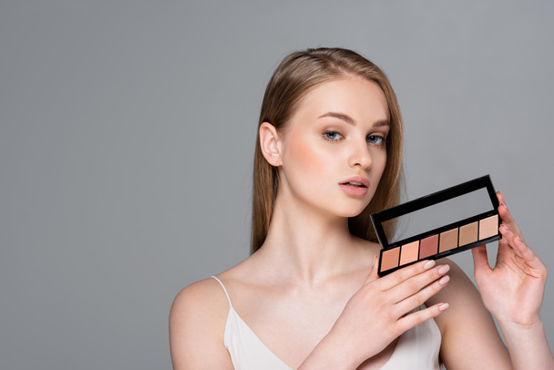 pretty young woman holding cosmetic palette isolated on grey - Foto, imagen