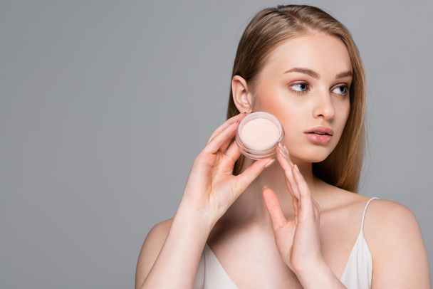 young woman holding face powder container isolated on grey - Foto, afbeelding