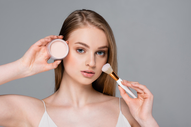 young woman holding cosmetic brush and face powder isolated on gray - Foto, immagini