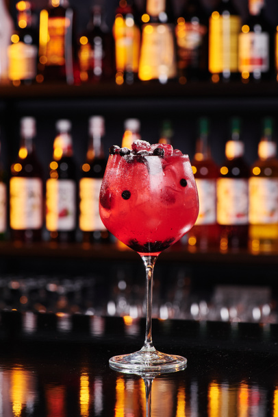 Red fruit cocktail in an elegant glass against the background of a bar in a nightclub. Space for text. - Photo, Image