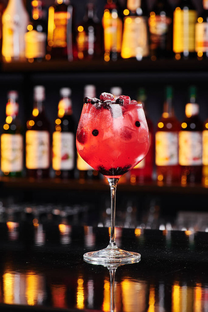 Roter Fruchtcocktail in einem eleganten Glas vor dem Hintergrund einer Bar in einem Nachtclub. Raum für Text. - Foto, Bild