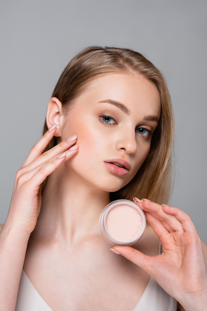 pretty blonde woman holding container with face powder isolated on grey - Foto, afbeelding