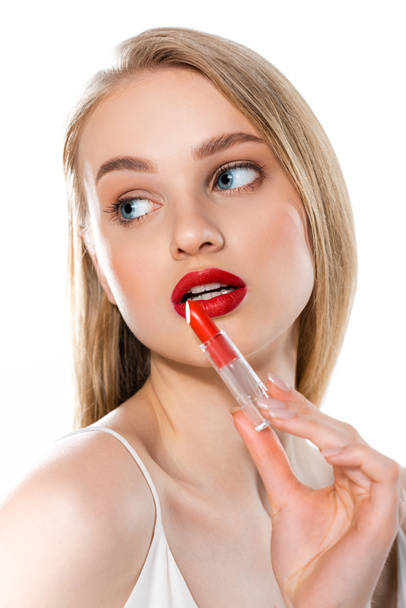 rubia joven con labios rojos y ojos azules sosteniendo tubo de lápiz labial aislado en blanco - Foto, Imagen