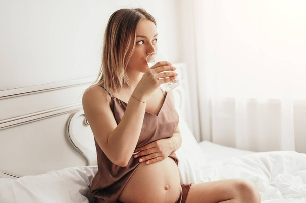 Pregnant woman drinking water on bed - Fotó, kép