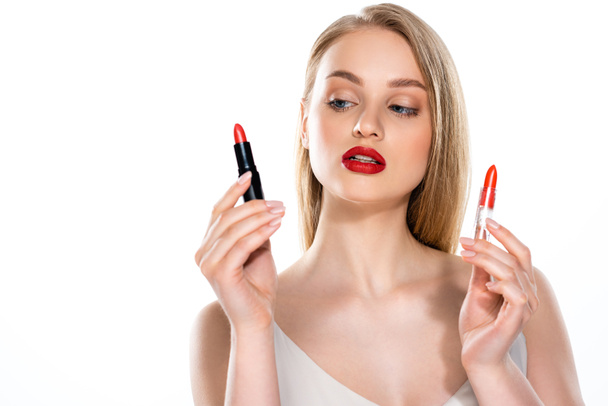 bonita joven con labios rojos sosteniendo tubos de lápiz labial aislados en blanco - Foto, Imagen