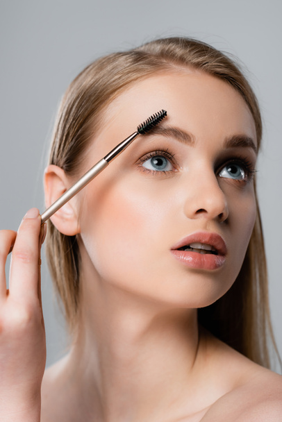 young woman with blue eyes styling eyebrow isolated on grey - Photo, Image