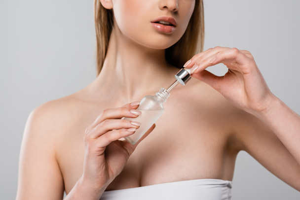 bijgesneden zicht op vrouw met blote schouders met fles met serum en pipet geïsoleerd op grijs - Foto, afbeelding