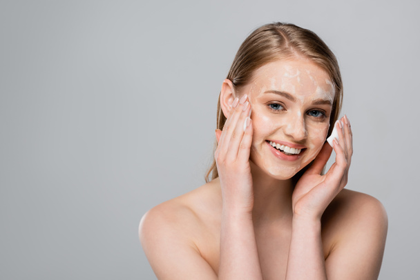 glückliche junge Frau mit blauen Augen und Reinigungsschaum im Gesicht isoliert auf grau - Foto, Bild
