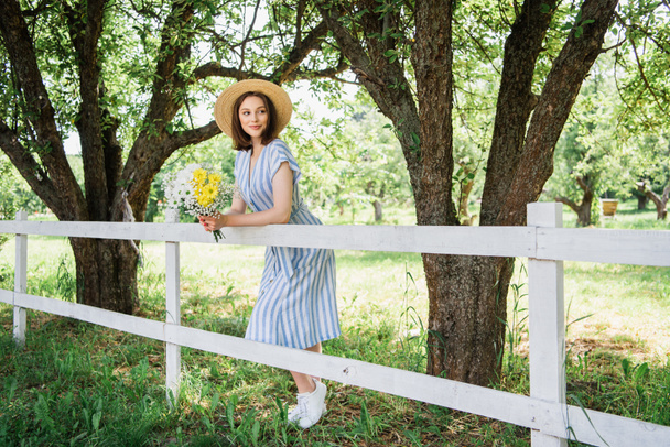 Gelukkig vrouw in jurk houden chrysanten in de buurt van hek in de zomer park  - Foto, afbeelding