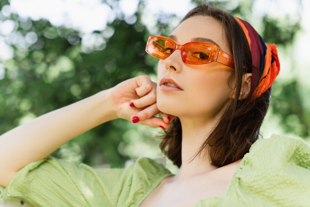 Niski kąt widzenia kobiety w okularach przeciwsłonecznych patrząc na kamerę na zewnątrz  - Zdjęcie, obraz