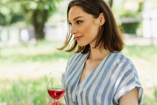 Young woman holding glass of wine in park  - Zdjęcie, obraz