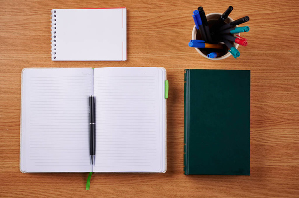 Notebooks abertos em branco liso com pilha de canetas dentro recipiente colocado em cima de uma mesa. Notepads revestidos vazios simples ao lado de um suporte de esferográficas coloridas em uma mesa. - Foto, Imagem
