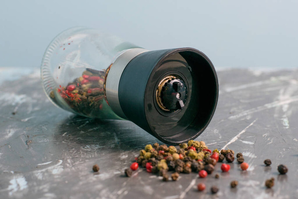 Pepper mill with mixture of peppercorns close up on dark concrete background. - 写真・画像