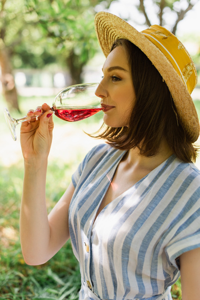 Side view of woman in sun hat drinking wine in park  - Foto, Imagem
