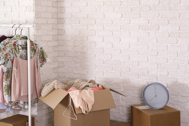 Bunch of blank unsigned moving boxes and clothing hanging on a rack in new empty apartment. Spacious unfurnished room with unpacked cardboard box stack. Interior background, copy space for text. - Фото, зображення