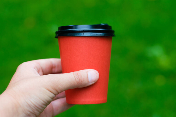 Verre avec café dans une main féminine sur le fond d'un parc, herbe verte et arbres. - Photo, image