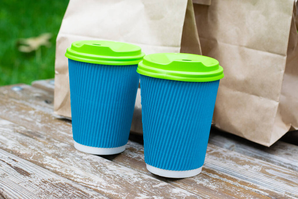 Paket poşet paket yiyecek ve parktaki bankta kahve bardakları. Yemek teslimatı kavramı, karantina sırasında iletişim 19.. - Fotoğraf, Görsel