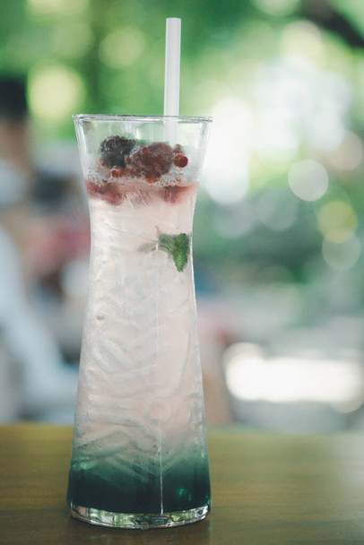 Склянка содового соку з льодом з прикрасою чорниці на столі та розмитим фоном зеленого дерева
 - Фото, зображення