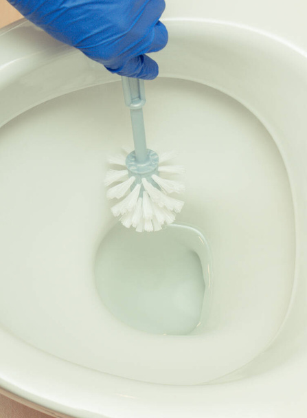 Hand of cleaner using brush for cleaning toilet in bathroom. Household duties concept - Φωτογραφία, εικόνα