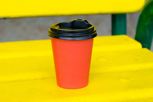 Papír csésze piros kávé soboyna sárga fa pad a strandon vagy a parkban a nyári napsütéses napon - Fotó, kép