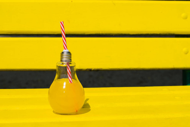 Свіжий апельсиновий сік або коктейль у скляній пляшці з соломою на жовтій дерев'яній лавці на пляжі або в парку
. - Фото, зображення