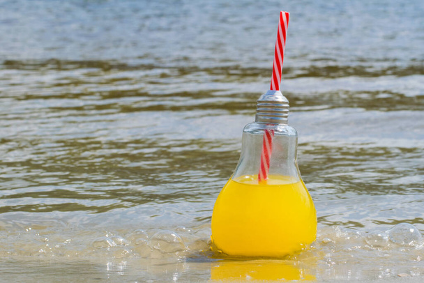 Fresco, limonada o cóctel en una botella de vidrio con un primer plano de paja en la arena de la playa cerca del agua. Concepto de viaje y recreación. - Foto, Imagen