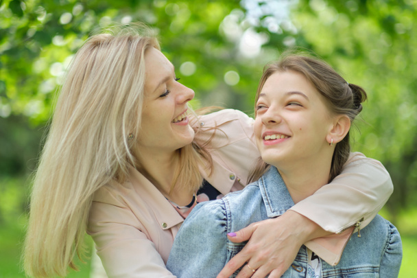 Eine glückliche Mutter mit ihrer Tochter, die im Sommer einen Teenager umarmt. Fürsorgliche glückliche Mutter genießen Tag mit Teenager-Mädchen Kind, lachen Spaß haben. Mutter gibt ihrer Tochter Rat. - Foto, Bild