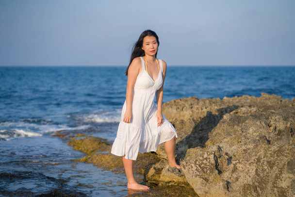 summer lifestyle portrait of young beautiful and happy Asian woman at the beach - Attractive Korean girl by the sea enjoying holidays trip on rock cliff with ocean view - Foto, Bild