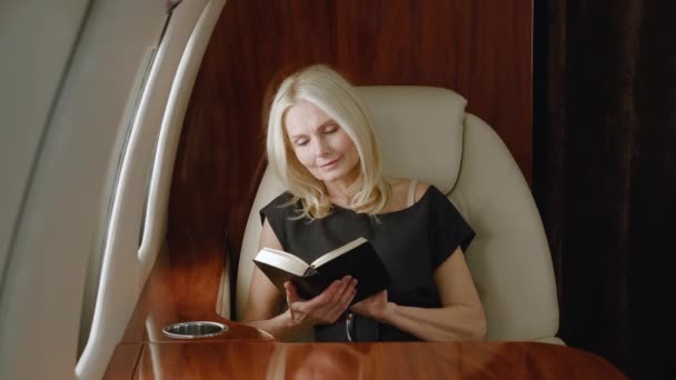 Krásná zralá bohatá žena čtení knihy nebo notebook při letu v soukromém letadle. Luxusní cestování soukromým tryskáčem. - Záběry, video