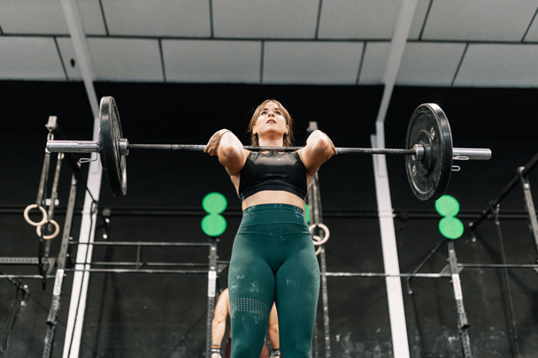Jonge fitness vrouw doet lange halter squats in een sportschool - Foto, afbeelding