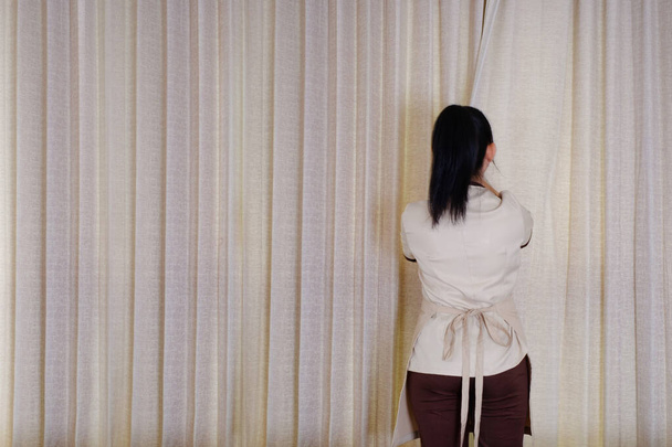 Hausmädchen schließt die Vorhänge am Fenster im Hotelzimmer  - Foto, Bild
