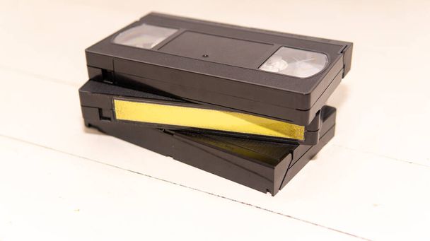 Uma pilha de três fitas VHS sobre uma superfície de madeira branca. Um deles tem uma etiqueta em branco. - Foto, Imagem