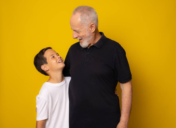 Grootvader en kleinzoon glimlachend over gele achtergrond - Foto, afbeelding