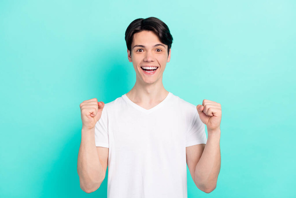 Photo portrait young guy wearing white t-shirt gesturing like winner isolated bright teal color background - Fotografie, Obrázek