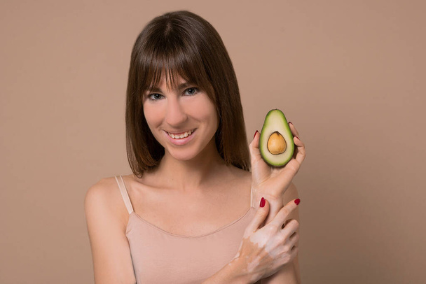 A slim long-haired woman in beige lingerie with avocado in her hands - Фото, изображение