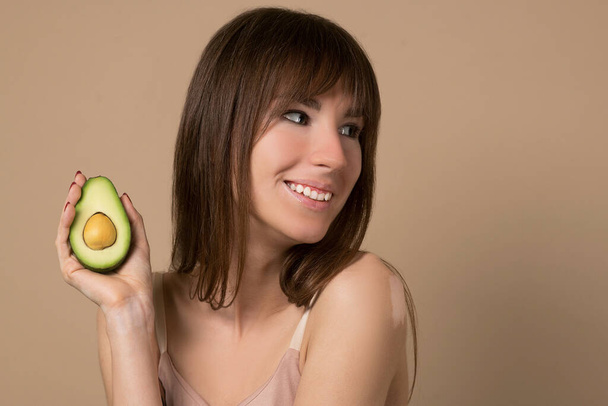 A slim long-haired woman in beige lingerie holding avocado - Photo, Image