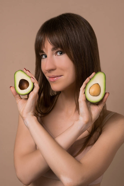 A slim long-haired woman in beige lingerie holding avocado - Foto, Imagen