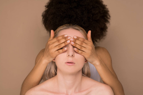 Egy sötét hajú nő becsukta a szemét egy szőke nő előtt. - Fotó, kép
