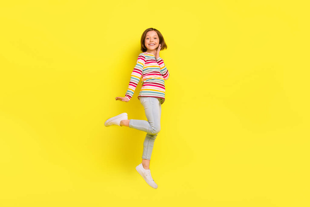 Full size foto van vrolijke korte kapsel klein meisje jump wear shirt broek sneakers geïsoleerd op gele kleur achtergrond - Foto, afbeelding