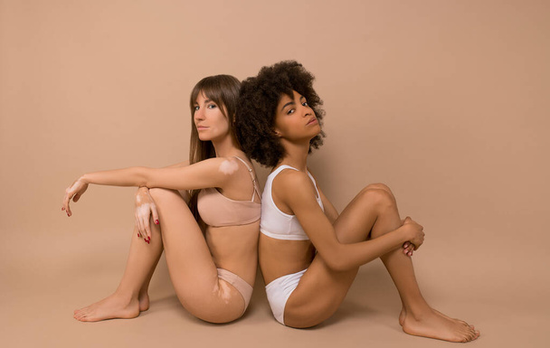 Две молодые женщины сидят спиной к спине и выглядят расслабленными - Фото, изображение